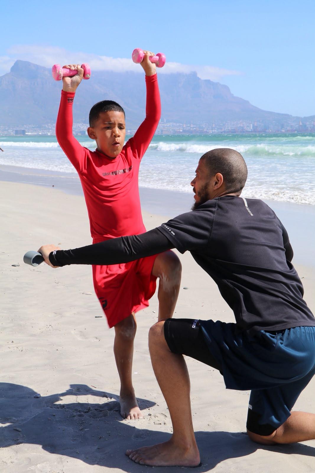 Overhead dumbbell press coached on the beach